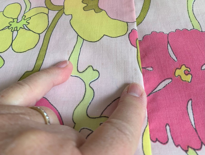 Op de afbeelding: Roze stof met een bloemenpatroon in tinten geel, groen en roze. De stof heeft een naad in het midden.