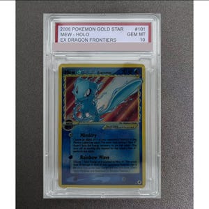 May include: A 2006 Pokemon Gold Star Mew trading card from the EX Dragon Frontiers set, graded GEM MT 10. The card features a blue Mew illustration, holographic foil, and text including Mimicry and Rainbow Wave attacks, encased in a clear slab.