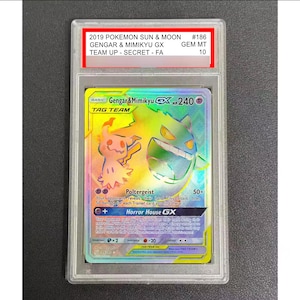 Könnte beinhalten: Eine bewertete Pokémon-Karte mit Gengar & Mimikyu GX aus dem 2019 Sun & Moon Team Up-Set. Die Karte hat ein holografisches Design mit Regenbogeneffekt und dem Text "Gengar & Mimikyu GX HP 240". Die Karte ist in einem Schutzhalter eingeschlossen.