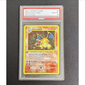 May include: A graded Charizard-Holo 1st Edition Pokémon card. The card features a yellow and orange Charizard illustration with the text "Charizard" and "120 HP". The card is encased in a clear protective holder with a "GEM MT 10" grade.