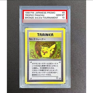 Op de afbeelding: Een Japanse 1998 Trophy Pikachu No. 3 Trainer ruilkaart, beoordeeld als GEM MT 10 door PSA. De kaart toont een gele Pikachu die een bronzen trofee vasthoudt tegen een metallic achtergrond, ingesloten in een doorzichtige, rechthoekige plastic houder.