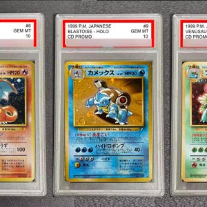 May include: Three graded Pokémon cards, including Charizard, Blastoise, and Venusaur, in clear plastic cases. Each case has a red label with card details and a Gem Mint 10 grade. The cards are from a 1999 Japanese CD Promo set.