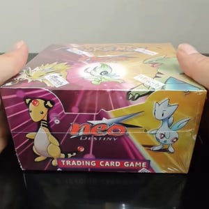 May include: A sealed Pokemon Neo Destiny trading card game booster box featuring colorful illustrations of various creatures including Ampharos and Togetic. The box has a purple and yellow design with the Neo Destiny logo printed on the front.