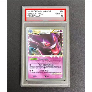 May include: A graded Pok&eacute;mon card featuring Gengar from the Triumphant set. The card has a purple Gengar illustration with a pink background. The card is encased in a clear protective holder with the text "2010 POKEMON HG & SS GENGAR - HOLO TRIUMPHANT".