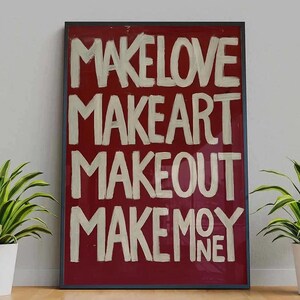 以下が含まれることがあります： 赤い背景に白い文字が書かれた、額入りのアートプリント。 「MAKE LOVE、MAKE ART、MAKEOUT、MAKE MONEY」という言葉が大胆な手書き風で表示されています。 フレームは暗く、アートワークはニュートラルな壁に展示されています。