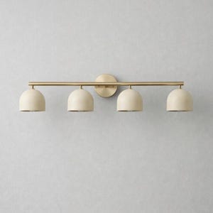 K&ouml;nnte beinhalten: Eine vierflammige Waschtischleuchte mit goldener Oberfl&auml;che. Die Leuchte hat vier cremefarbene, kuppelf&ouml;rmige Schirme. Das Licht ist an einer goldenen Stange und einer kreisf&ouml;rmigen Wandplatte befestigt.