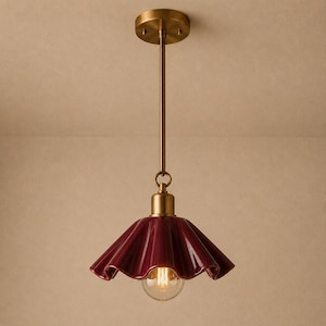 May include: A pendant light fixture featuring a deep burgundy, ruffled ceramic shade suspended from a brass-toned metal rod and circular ceiling canopy. The design includes a single exposed glass light bulb centered beneath the flared shade.