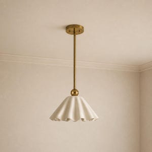 May include: A pendant light fixture featuring a brass-toned metal rod and a circular ceiling mount. The fixture includes a spherical brass connector attached to a wide, off-white, fluted ceramic shade with a scalloped edge design.