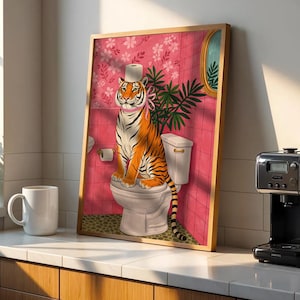 May include: A framed art print featuring a tiger sitting on a toilet. The tiger wears a toilet paper hat and a pink ribbon. The background is a pink tiled wall with floral wallpaper and a mirror. The art print is in a wooden frame.