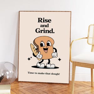Könnte beinhalten: Ein gerahmter Kunstdruck mit einem lächelnden Cartoon-Brot-Charakter, der ein Baguette hält und einen Daumen hoch zeigt. Der Text "Rise and Grind" und "Time to make that dough!" ist in Schwarz dargestellt.