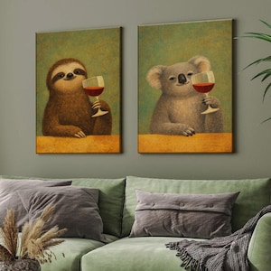 Könnte beinhalten: Zwei gerahmte Leinwandkunstdrucke. Einer zeigt ein Faultier mit einem Glas Rotwein, der andere einen Koala mit einem Glas Rotwein. Beide Tiere sind vor einem grünen Hintergrund mit einer gelb-orangen Basis dargestellt.