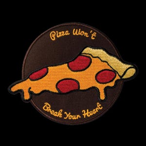 May include: Embroidered patch featuring a pizza slice with pepperoni on a brown circular background. The patch has the text "Pizza Won't Break Your Heart" in yellow script. The pizza slice is orange, yellow, and red.