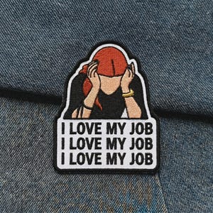 May include: Embroidered patch with the phrase "I LOVE MY JOB" repeated three times. The patch features a woman with red hair, hands on her head, and a black top. The patch is on a blue denim background.