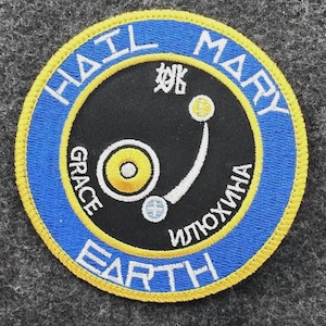 May include: A circular patch with a blue border and yellow trim. The text "HAIL MARY EARTH" is in white. The center is black with white and yellow graphics and text in Chinese and Russian.