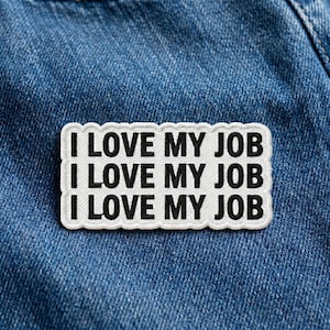 May include: A white patch with black text that reads "I LOVE MY JOB" repeated three times. The patch has a white border and is set against a blue denim background.