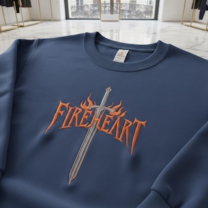 May include: A navy blue sweatshirt featuring an embroidered design. The design includes the word "FIREHEART" in orange, with a sword and flames. The sweatshirt has a crew neck and long sleeves.