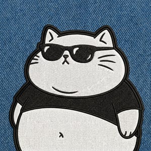 May include: Embroidered patch featuring a cartoon cat wearing black sunglasses and a black shirt. The cat is white with black outlines and details, including whiskers and a belly button. The patch is set against a blue denim background.