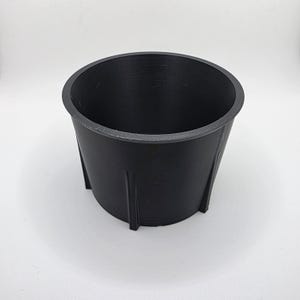 Peut inclure: Un récipient cylindrique noir mat doté d'un large bord circulaire et de quatre nervures structurelles verticales régulièrement espacées sur la paroi extérieure. L'objet présente une finition lisse et uniforme ainsi qu'un intérieur creux.