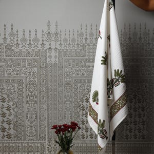 Peut inclure: Une serviette blanche à texture gaufrée ornée d'un motif répétitif de feuilles vertes rappelant des palmes et de petites touches rouges. La serviette présente une bordure décorative à motif floral vert et rouge sur le bord inférieur.