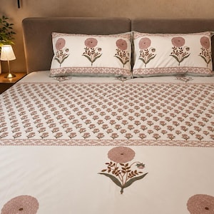 Puede incluir: Una colcha blanca y dos fundas de almohada a juego con un patrón repetitivo de pequeñas flores rosas con tallos verdes. El juego de cama incluye un borde más ancho con motivos florales rosas más grandes y un adorno geométrico en los bordes.