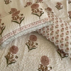 May include: Cream-colored bedding set with a floral pattern. The set includes two rectangular pillowcases and a quilt. The pillowcases feature a large floral design with pink and green accents. The quilt has a repeating floral pattern.