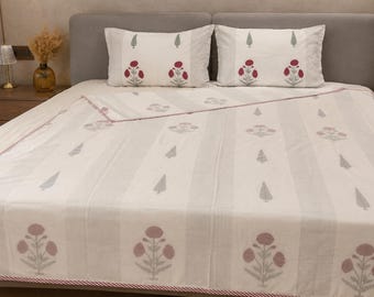 May include: A white bedspread and two matching pillowcases featuring a repeating pattern of red floral motifs and grey leaf designs. The fabric has vertical stripes and a thin red and white striped border along the edge of the bedspread.