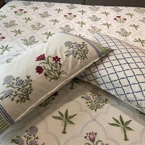 Peut inclure: Un drap de lit blanc et deux taies d'oreiller avec un motif répétitif de fleurs rouges et violettes et de plantes vertes ressemblant à des palmiers. Une taie présente un quadrillage bleu, l'autre assortie au drap avec des rayures.