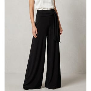 May include: Solid black high-waisted wide-leg trousers featuring a thick, integrated fabric waistband that ties at the side. The pants have a relaxed, flowing silhouette that extends to the floor, crafted from a smooth, opaque material.