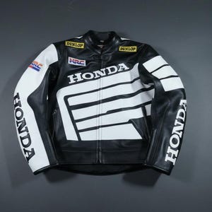 Peut inclure: Veste de course de moto Honda noire et blanche. La veste présente le logo Honda sur la poitrine et les manches, avec des rayures et des accents blancs. La veste a une fermeture éclair et plusieurs écussons.