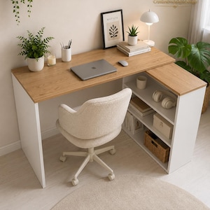 May include: An L-shaped desk with a light wood grain top and white side panels, featuring integrated open shelving on one side. A cream-coloured upholstered swivel chair with wheels is positioned in front of the desk, which holds a laptop, mouse, books, a small lamp, and a framed Matisse print.