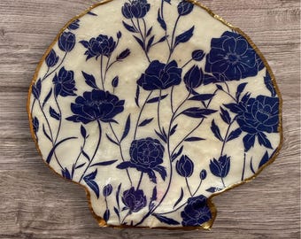Adorno de joyería hecho a mano con flores azules sobre concha de vieira.