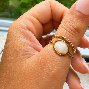 Può includere: Un set di due anelli color oro. Un anello presenta una fascia testurizzata con perline. Il secondo anello ha una fascia intrecciata e un'incastonatura centrale ovale contenente una pietra druzy bianca cristallina dalla superficie ruvida.