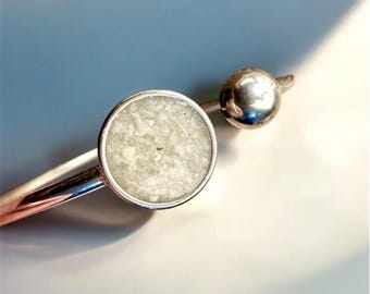 Può includere: Un fermaglio per capelli argentato con un'incastonatura circolare in pietra chiara e un piccolo dettaglio sferico. Il fermaglio ha un design elegante e moderno, ideale per fissare i capelli. L'incastonatura della pietra ha un aspetto maculato.