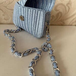 May include: A pale blue woven handbag with a silver chain strap. The bag is rectangular with a flap closure and a silver clasp. The chain strap combines silver links and pale blue woven material.