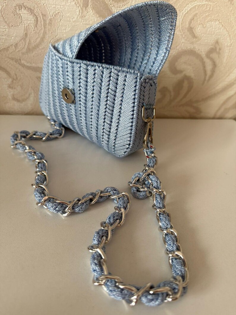 May include: A pale blue woven handbag with a silver chain strap. The bag is rectangular with a flap closure and a silver clasp. The chain strap combines silver links and pale blue woven material.