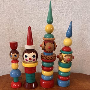 May include: Four stacked wooden toy figures in varying heights, featuring colorful geometric shapes including spheres, cones, and rings in red, yellow, blue, green, and brown. Each figure is constructed from multiple interlocking components.