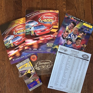 Può includere: Una collezione di cimeli NASCAR, tra cui programmi souvenir, una guida per i fan e un biglietto. I programmi presentano auto da corsa e il logo "Banquet 400". La guida per i fan mostra le foto dei piloti. Il biglietto è per il Kansas Speedway.