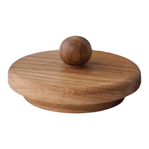 May include: A circular wooden lid featuring a small, spherical knob. The lid is crafted from light brown wood, displaying prominent grain patterns, while the knob is a darker shade of brown. This design is simple and natural, ideal for kitchen or home decor.