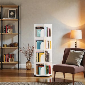 May include: A white, rotating bookshelf filled with books of various sizes and colors. The bookshelf has four tiers and is positioned in a living room setting. A wooden and metal shelf is visible in the background, along with a brown armchair and a lamp.