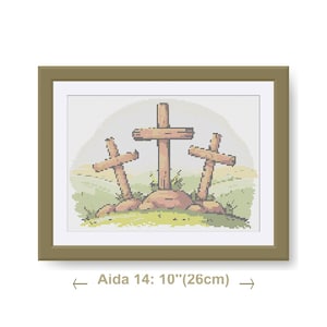 May include: A framed cross-stitch artwork showing three wooden crosses on a grassy hill. The artwork is framed in a brown frame and measures 26cm wide. The background features a light-coloured sky.