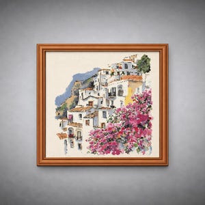 Puede incluir: Obra de arte en punto de cruz enmarcada que representa un pueblo costero. Edificios blancos con tejados de terracota descienden por una ladera, acentuados por vibrantes plantas de flores rosas. La obra está en un marco de madera marrón.