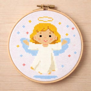 Può includere: Un disegno di angelo a punto croce in un telaio da ricamo in legno. L'angelo ha capelli gialli, un'aureola e ali blu, indossa una veste bianca. Lo sfondo è bianco con piccoli accenti di stelle colorate.