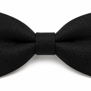 May include: A black bow tie with a textured fabric. The bow tie is centered and has a classic butterfly shape. The background is plain white.