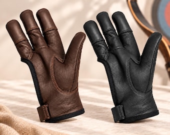 May include: Two archery finger gloves, one in dark brown leather and one in black leather. Each glove features three reinforced finger stalls, a textured leather palm, and a hook-and-loop closure strap at the wrist for a secure fit.