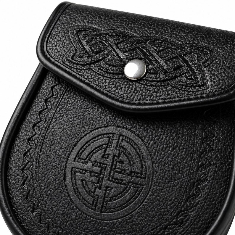 May include: Black leather sporran with embossed Celtic knot designs and a circular emblem. It has a flap closure with a silver button and decorative stitching. The leather has a textured finish. The sporran is a traditional Scottish accessory.