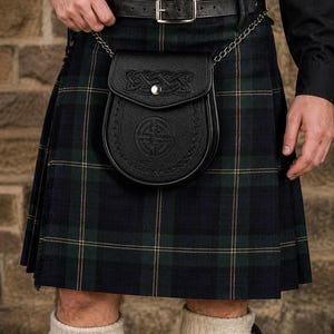 May include: A Scottish kilt in a green, navy, and tan plaid design. A black leather sporran, featuring Celtic knot and circular patterns, is suspended by a chain from a black leather belt. The kilt is worn with white socks.