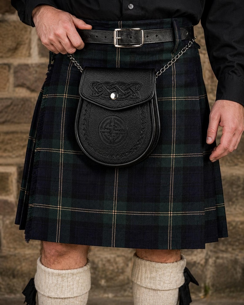 May include: A Scottish kilt in a green, navy, and tan plaid design. A black leather sporran, featuring Celtic knot and circular patterns, is suspended by a chain from a black leather belt. The kilt is worn with white socks.