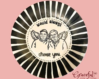 May include: A decorative ceramic plate with a black and white striped border. The center features a hand-drawn illustration of two figures with angel wings, and the text "would always choose you."