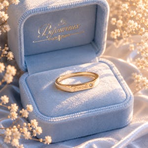 May include: A gold ring with the word "fuck" engraved on it, set in a light blue velvet ring box. The ring features a small diamond. The ring box has the word "Bijourans" in gold lettering.