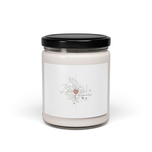 May include: A white candle in a glass jar with a black lid. The label features a map design with a heart and the text "Home is Where The Heart Is."